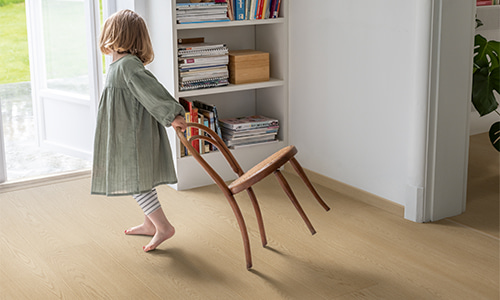 ребенок тянет стул по бежевому ламинату